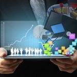 Photo of two hands holding a tablet horizontally with illustrations of graphs and icons floating off the face of the tablet.