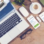 A photo showing a top-down view of a laptop and its screen, a computer mouse, cell phone, and tablet. All of the screens show the AlertBot.com website. A cup of hot coffee is also on the desk with other office items.