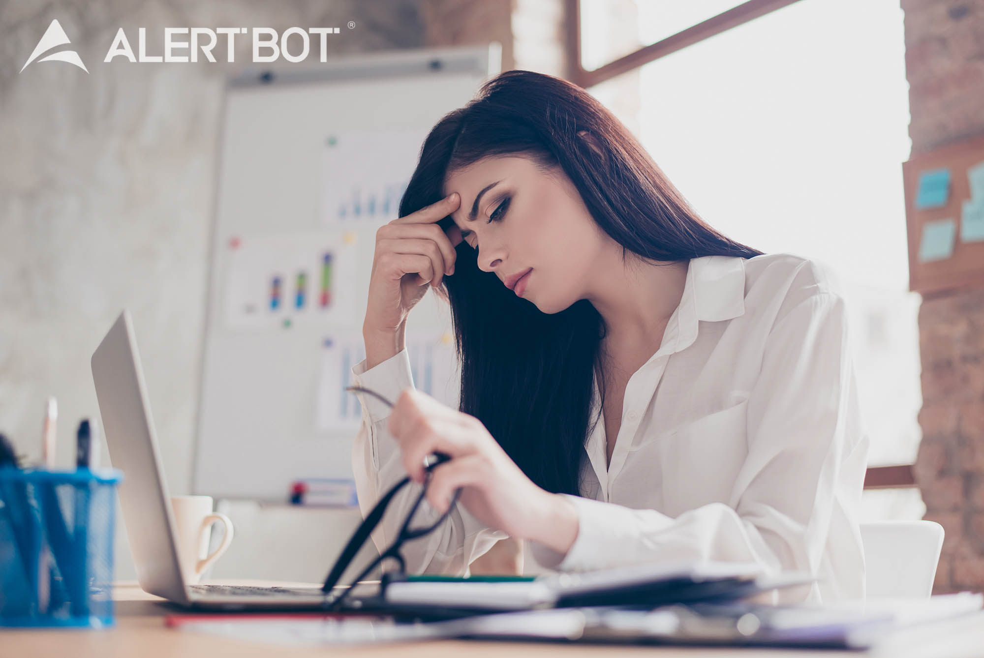 A beautiful woman with brown hair and her right hand to her forehead looking concerned. Her left hand is holding her glasses. She's looking down at her laptop. A chart with graphs is in the background.