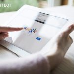 AlertBot blog titled "How Site Uptime Impacts SEO (Hint: It&rsquo;s a REALLY Big Deal)" with photo of a woman's hands pointing at a web browser featuring Google on an iPad tablet.