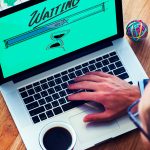 AlertBot Blog titled "Just How Bad is a Down, Slow, or Dysfunctional Website? It&rsquo;s Worse than You Think!" with an aerial view of a man with his hand on a laptop keyboard with the word "Waiting" and an hourglass on the monitor screen.