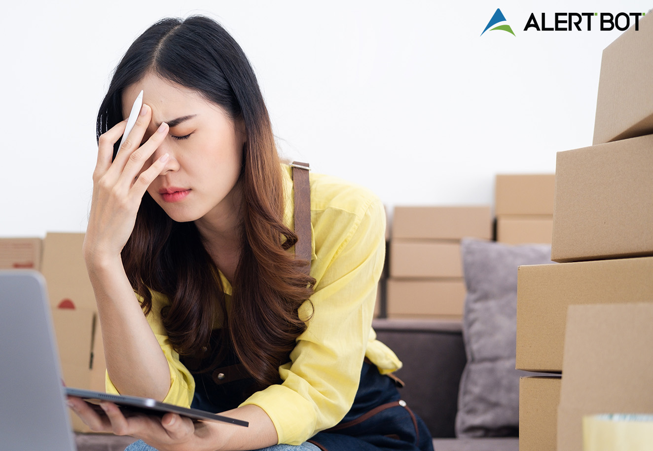 AlertBot Blog titled "7 Deadly e-Commerce Checkout Sins" with the photo of an Asian woman sitting at a laptop with a tablet in one hand and her face in the palm of the other hand looking distressed.