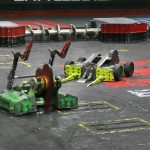 Battlebots Whiplash fighting with another robot. Green robot with metal arms up with Whiplash yellow robot preparing for attack in Battlebots arena