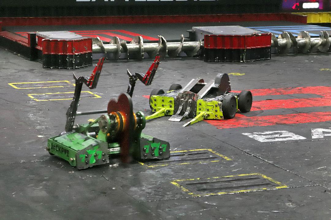 Battlebots Whiplash fighting with another robot. Green robot with metal arms up with Whiplash yellow robot preparing for attack in Battlebots arena